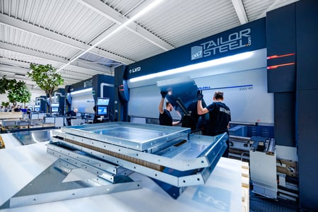 "Medewerkers van 247TailorSteel bewerken metaal, met stapels onderdelen op de voorgrond."